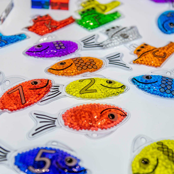 Rainbow Gel Number Fish, Vibrantly rainbow coloured Rainbow Gel Number Fish with numbers 0-20 on one side and their corresponding dots on the other. The Rainbow Gel Number Fish are Ideal for learning to count, to associate numbers with quantities, for colour recognition and for sensory play. The tactile squashy Rainbow Gel Number Fish contain gel-like beads in 7 crystal clear rainbow colours, with a loop at the top for hanging on a string or with pegs. The translucent colours contained within the Rainbow Ge